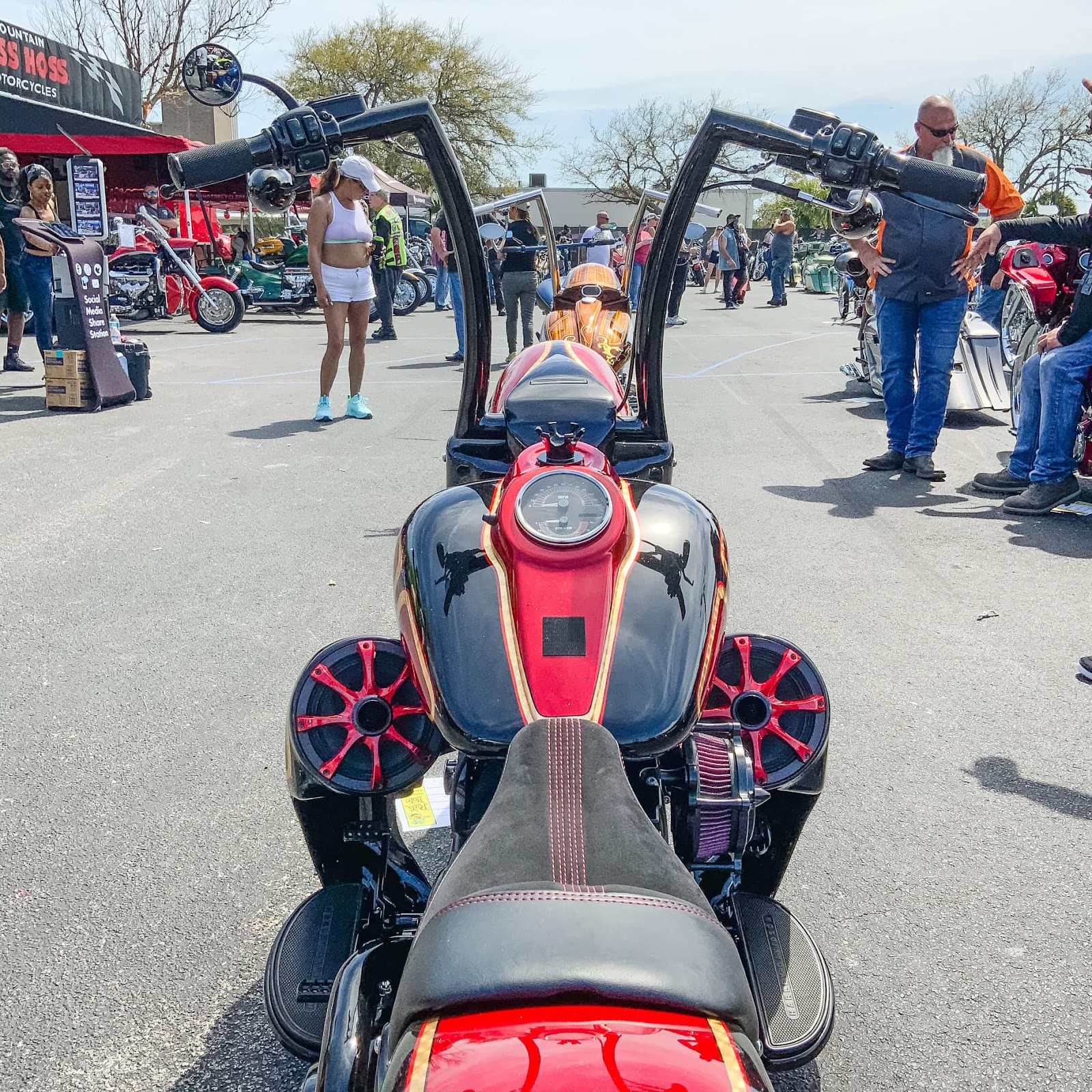 A rider point of view of a red chopper, with high handlebars and speaker sound systems installed by the foot pegs.