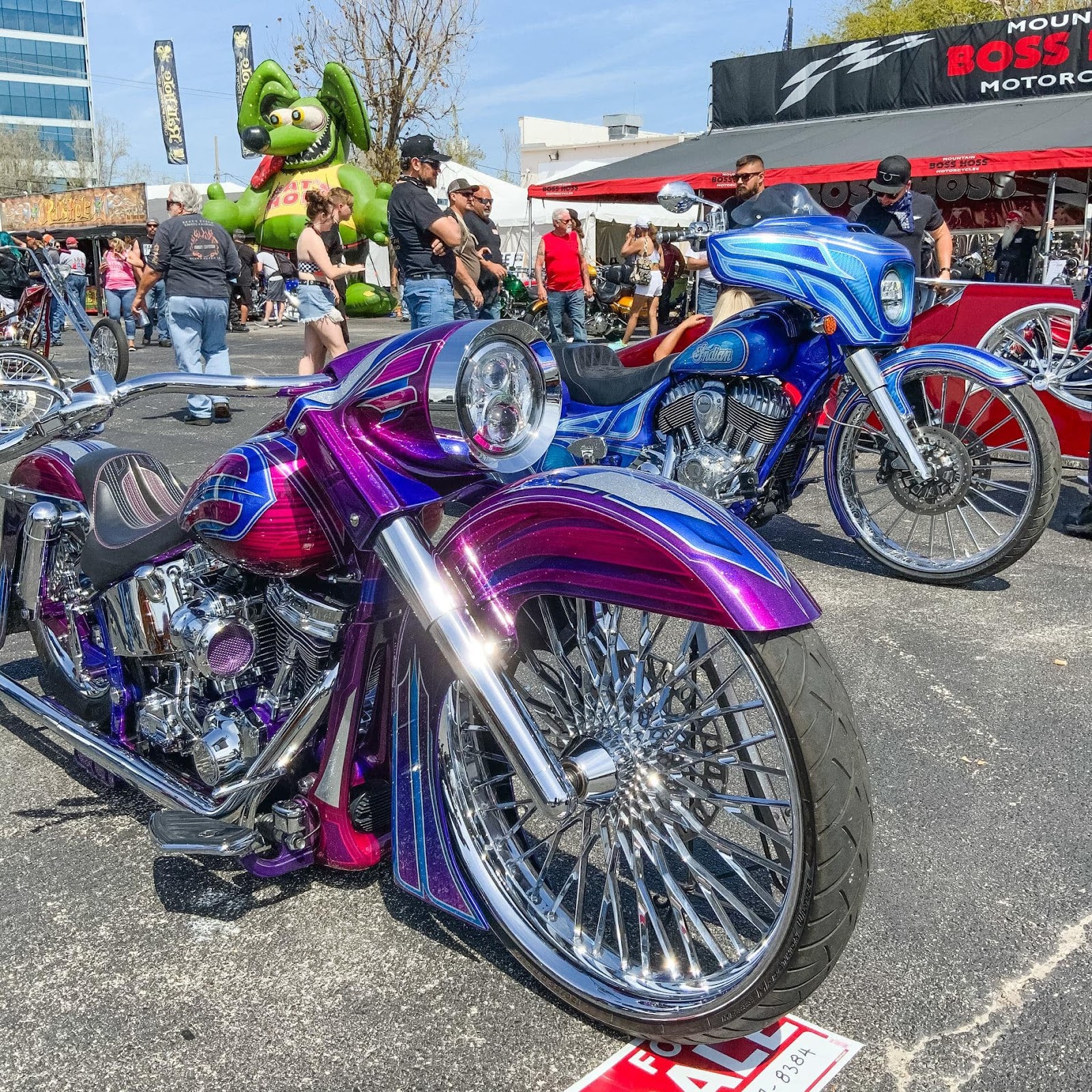 A sparkling fuchsia chopper low rider with shiny chrome details and a matching blue sparkly motorcycle customized in the background.