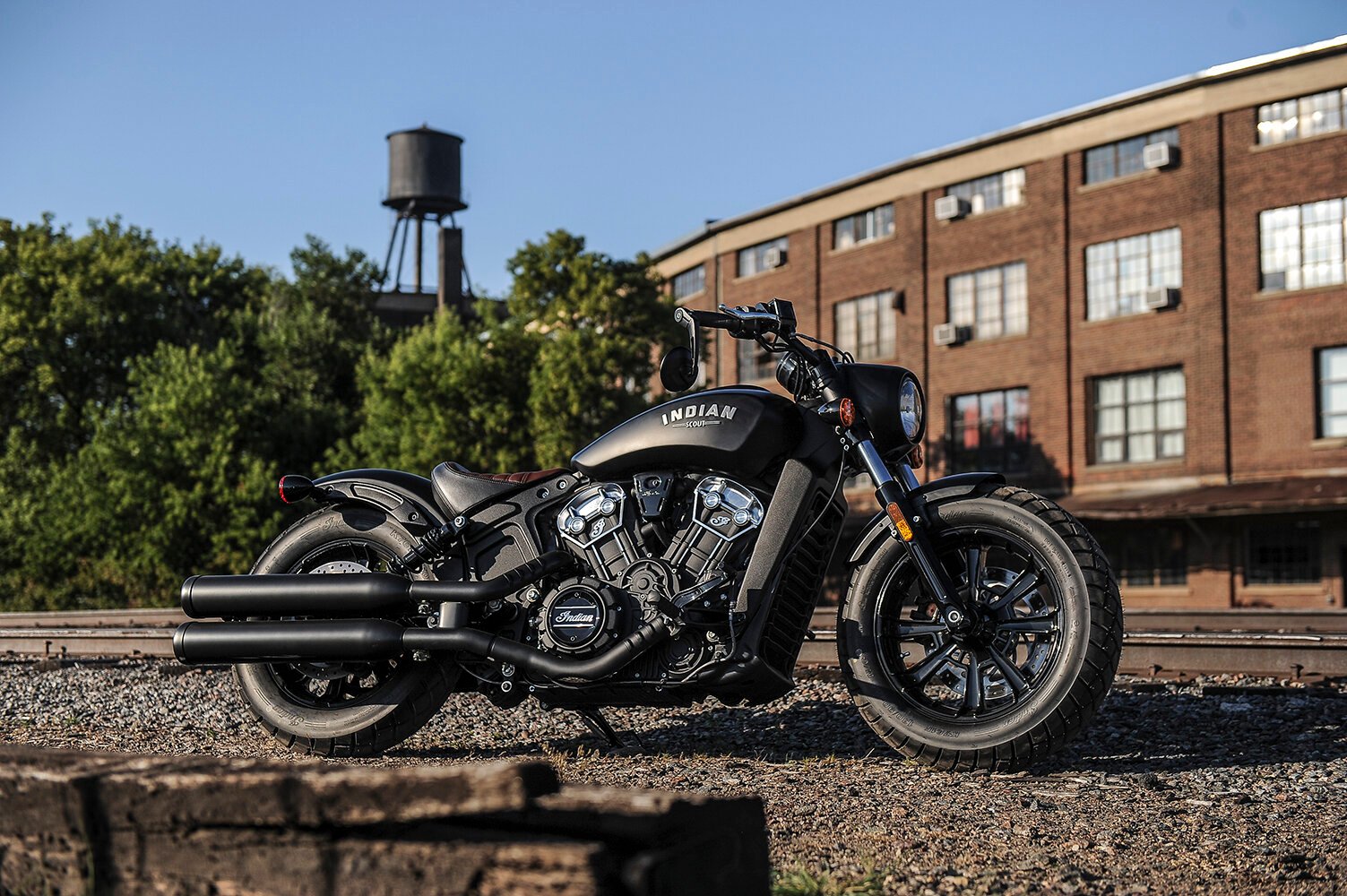 All black Indian Scout Bobber parked next to train tracks - a sleek and powerful motorcycle perfect for cruising through urban and rural landscapes