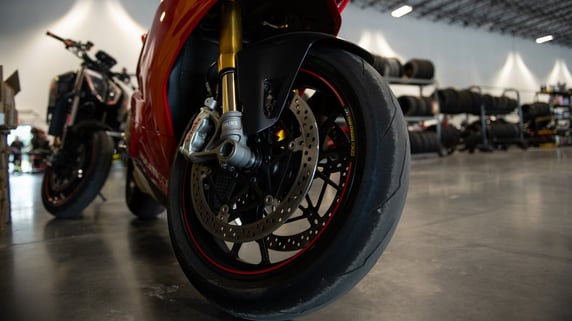 A red motorcycle's newly upgraded front tire is shown, with new tires in the background. 