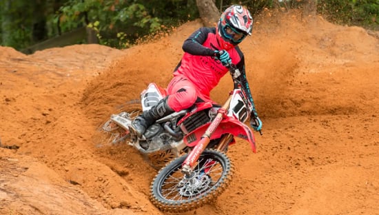 Dirt biker in full protective gear, dynamically kicking up dust while riding on a trail