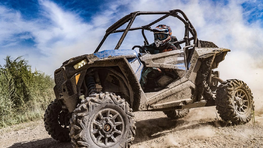 A muddied ATV being driven on a dirt off-road. When ATV's get too muddy, you should maintain them by giving them a wash.