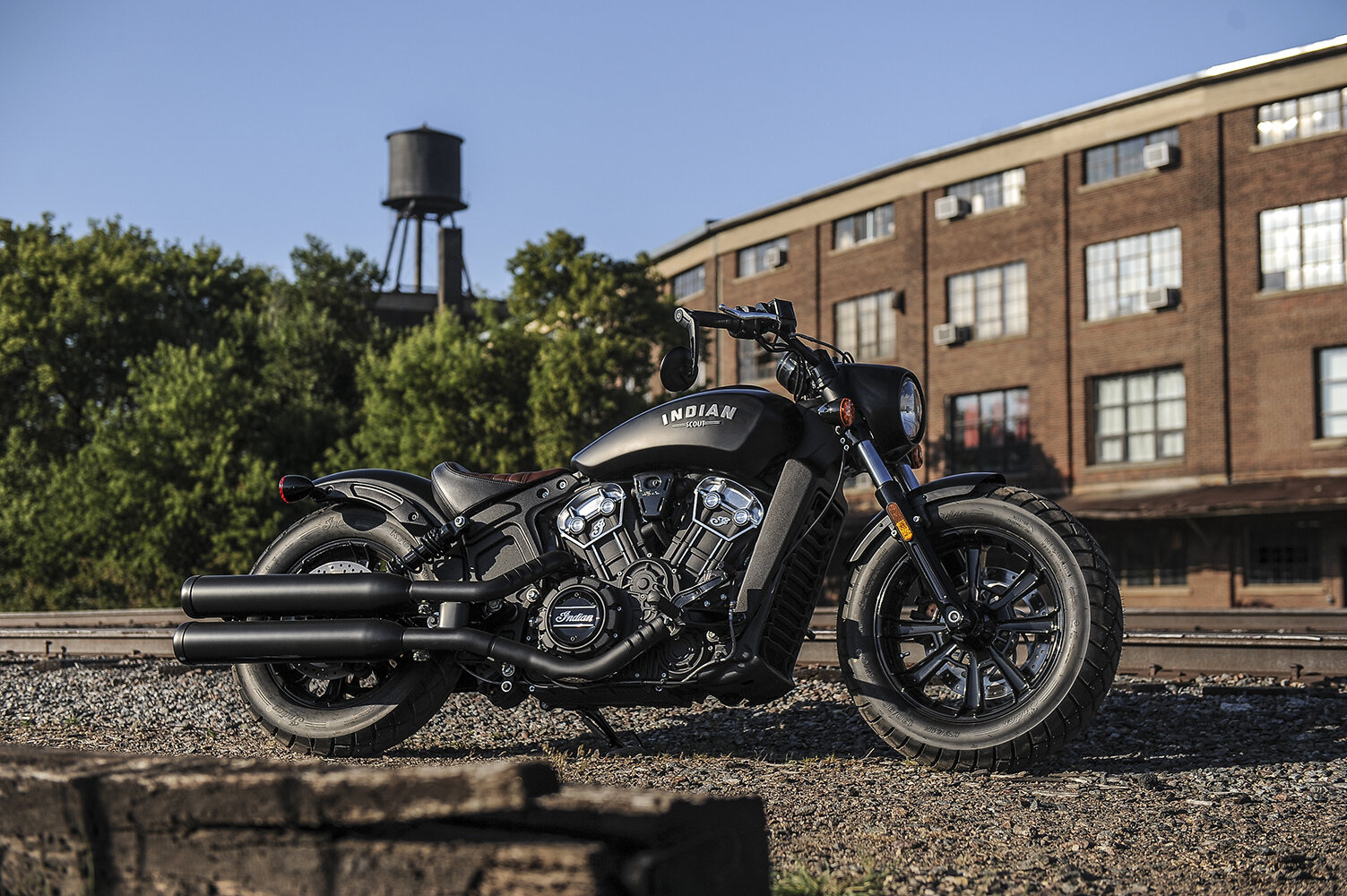 All black Indian Scout Bobber parked next to train tracks - a sleek and powerful motorcycle perfect for cruising through urban and rural landscapes