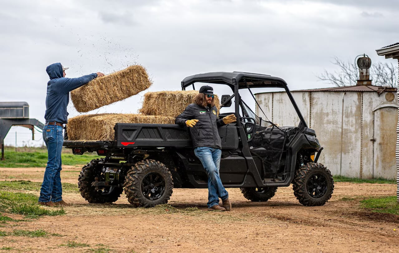 Two farmers loading hay bales onto the cargo bed of the best UTV for farm work