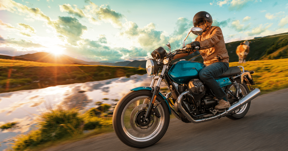 Motorcyclist riding on snow-free highway at sunset amidst lush greenery