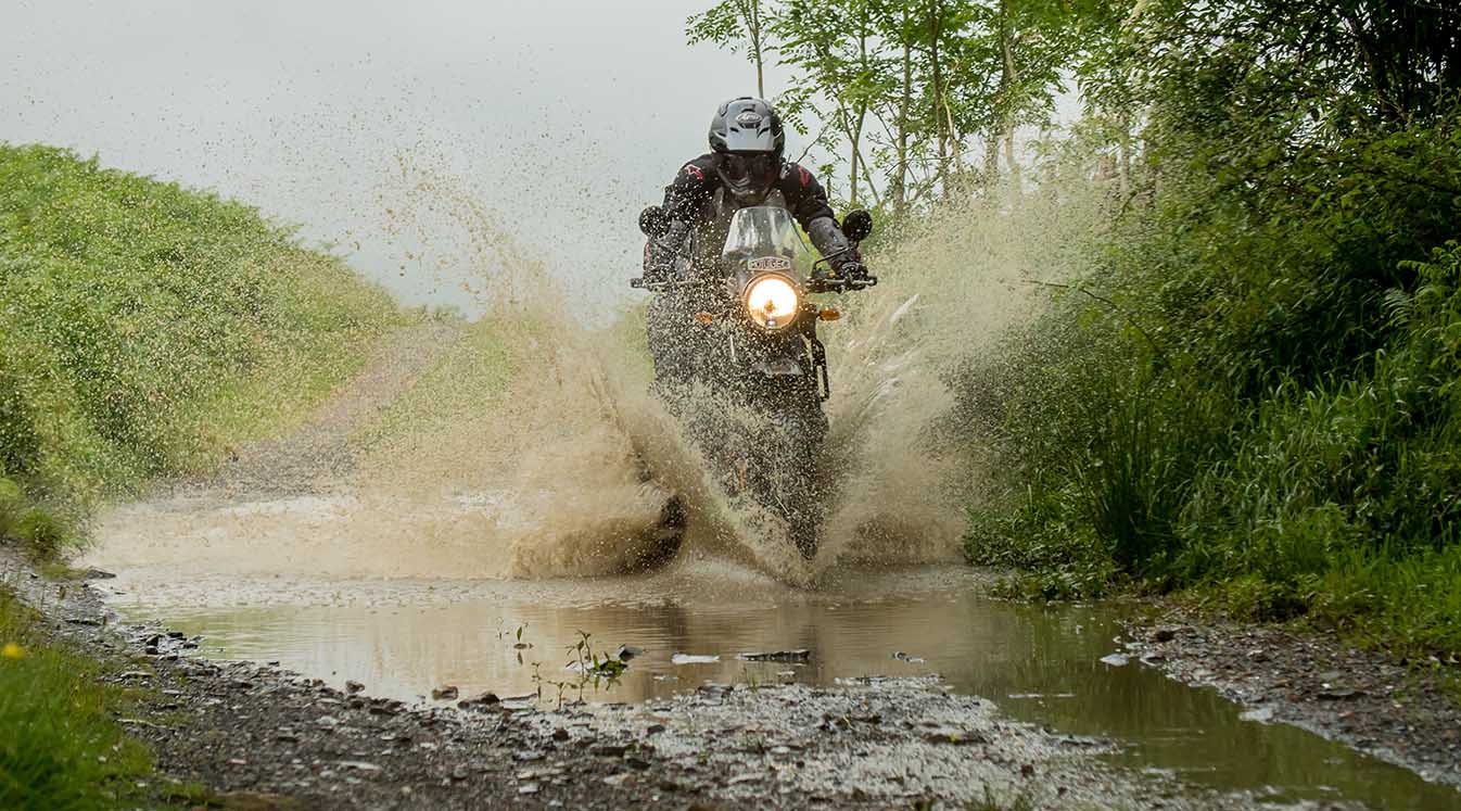 Motorcyclist riding through water on dirt trail