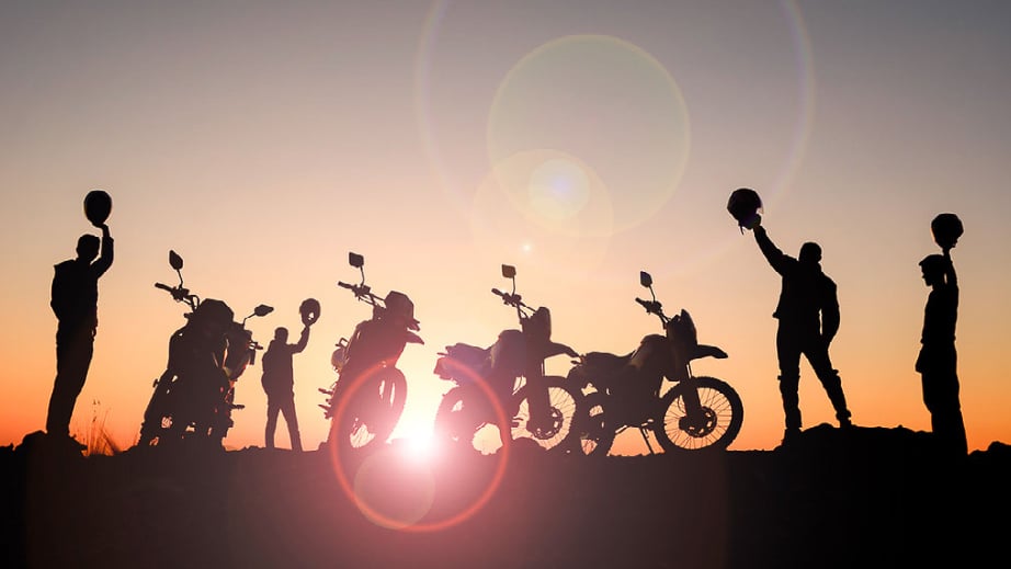 A group of young adult millenial motorcycle riders posing at sunset, as they are a silhouette. 